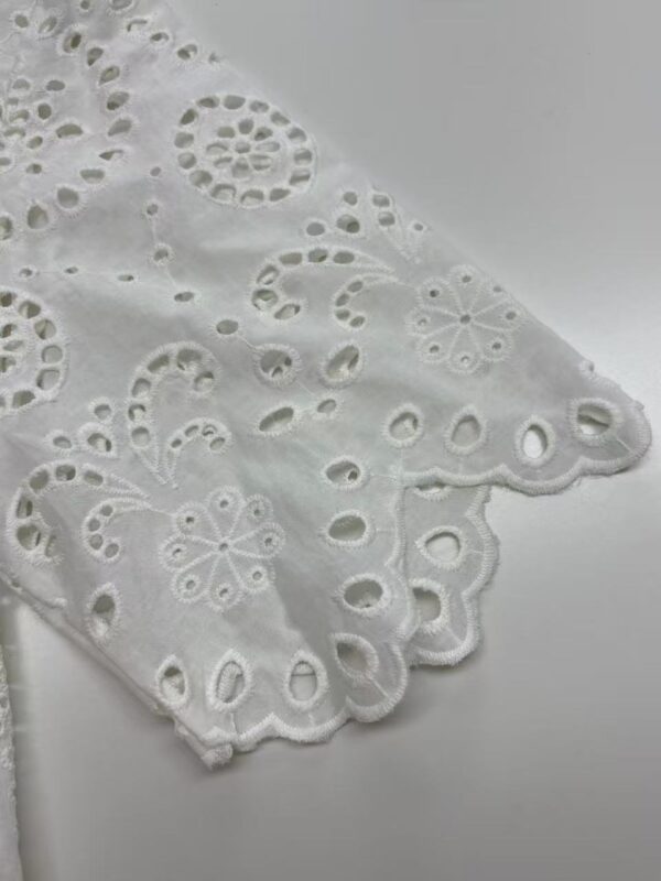 Close-up of white eyelet lace fabric with floral and circular patterns, showcasing intricate embroidery and scalloped edges.