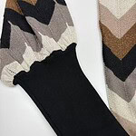 Close-up of a knit sweater featuring a chevron pattern in beige, brown, black, and cream with a black cuff detail, showcasing stylish winter fashion.