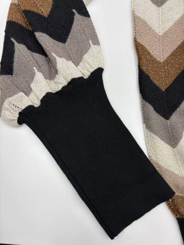 Close-up of a knit sweater featuring a chevron pattern in beige, brown, black, and cream with a black cuff detail, showcasing stylish winter fashion.