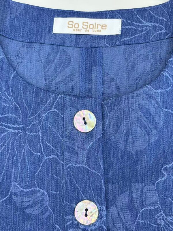 Close-up of a blue dress with a subtle floral pattern and a button-up front, showcasing a stylish and luxurious design.
