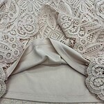 Close-up of intricate lace fabric combined with smooth beige leather, showcasing detailed craftsmanship and luxurious texture for fashion accessories or clothing.