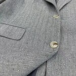 Close-up of a stylish grey herringbone blazer with two buttons, tailored for a sophisticated look, perfect for formal or business attire.