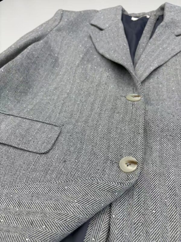 Close-up of a stylish grey herringbone blazer with two buttons, tailored for a sophisticated look, perfect for formal or business attire.
