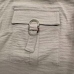 Close-up of a stylish beige fabric pocket with a metal ring and fabric strap, showcasing modern design elements for women's fashion.