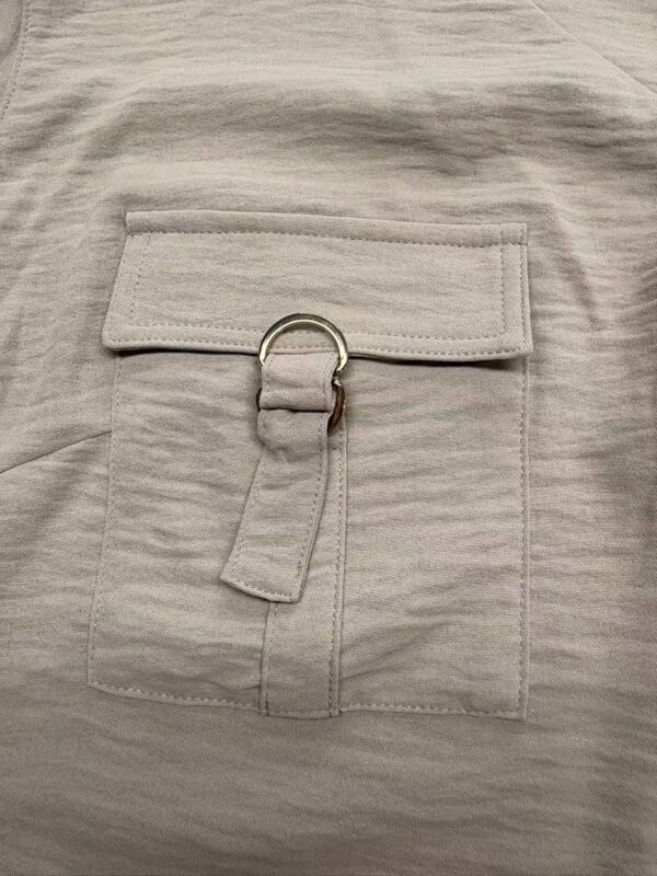 Close-up of a stylish beige fabric pocket with a metal ring and fabric strap, showcasing modern design elements for women's fashion.