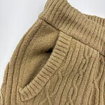 Close-up of a beige cable knit sweater with a ribbed collar and a side pocket, perfect for autumn fashion.
