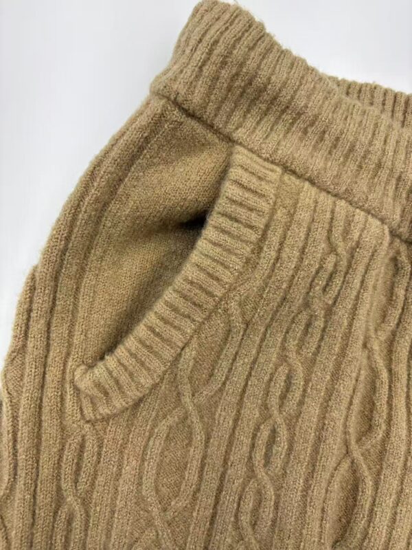 Close-up of a beige cable knit sweater with a ribbed collar and a side pocket, perfect for autumn fashion.