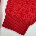 Close-up of a red knitted sweater cuff with textured and ribbed design, showcasing warmth and comfort for winter fashion.