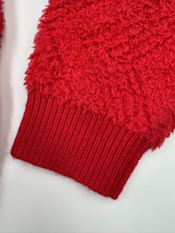 Close-up of a red knitted sweater cuff with textured and ribbed design, showcasing warmth and comfort for winter fashion.