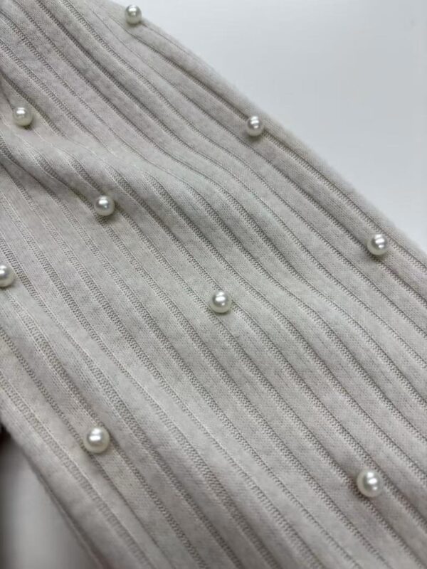Close-up of beige fabric with vertical stripes and scattered pearl embellishments, showcasing luxury textile design.
