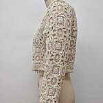 Close-up of a cream-colored crochet jacket with intricate patterns, displayed on a mannequin against a plain background.