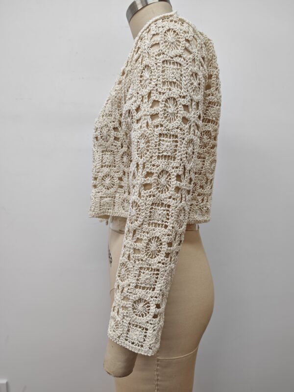 Close-up of a cream-colored crochet jacket with intricate patterns, displayed on a mannequin against a plain background.