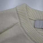 Close-up of a cream-colored knit sweater showing detailed stitching and ribbed collar, perfect for fashion and clothing SEO.