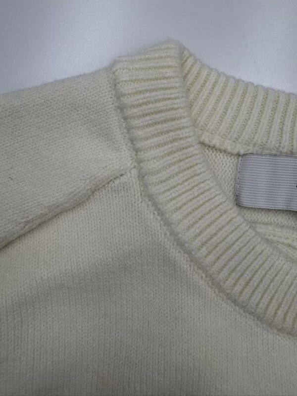 Close-up of a cream-colored knit sweater showing detailed stitching and ribbed collar, perfect for fashion and clothing SEO.