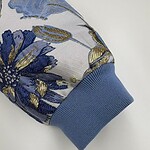 Close-up of a sleeve with intricate floral embroidery in blue, gold, and silver threads, featuring a light blue ribbed cuff.