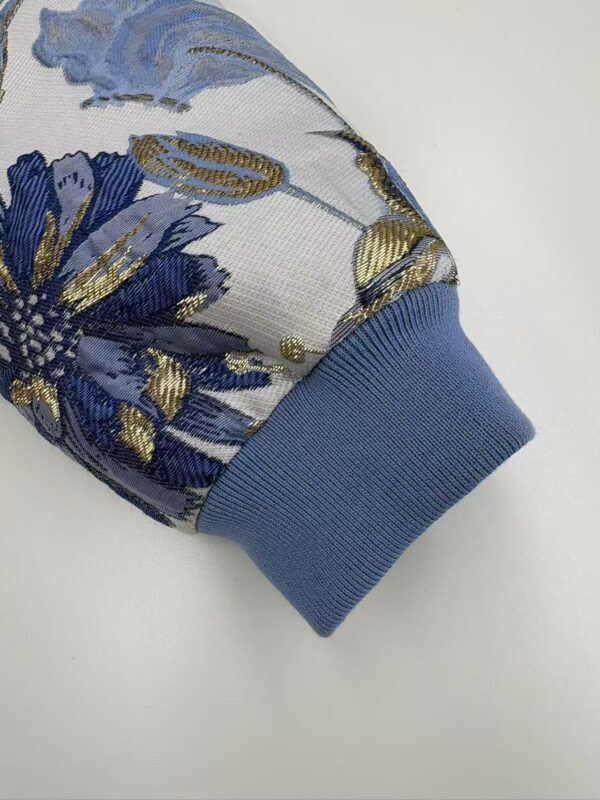 Close-up of a sleeve with intricate floral embroidery in blue, gold, and silver threads, featuring a light blue ribbed cuff.