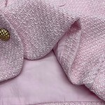 Close-up of a pink tweed women's jacket with gold button details, showcasing textured fabric and stylish design.