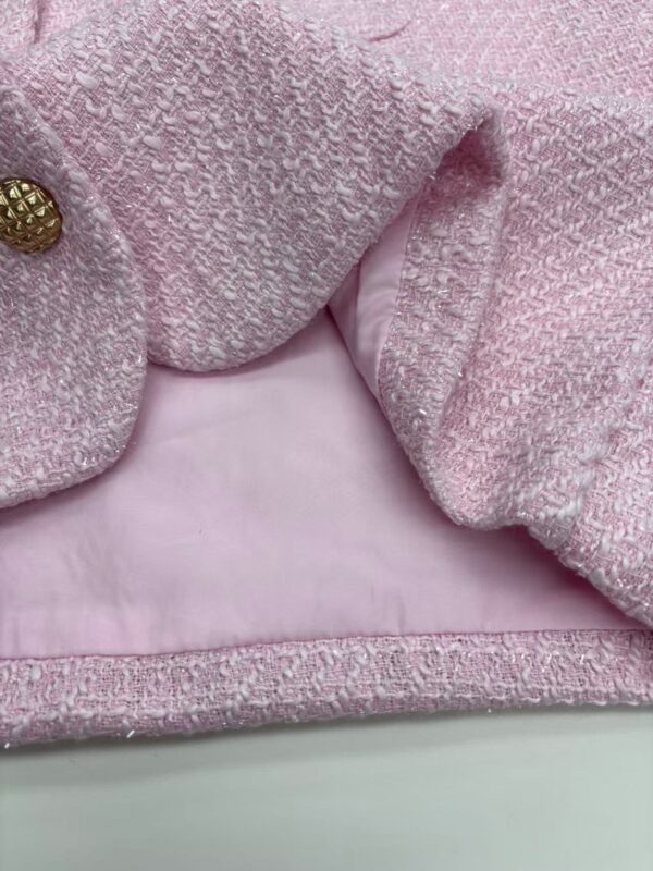 Close-up of a pink tweed women's jacket with gold button details, showcasing textured fabric and stylish design.