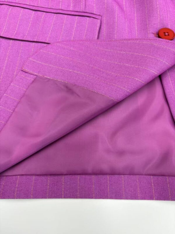 Close-up of a pink pinstripe women's suit jacket with a red button, showing detailed fabric texture and lining.