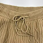 Close-up of a beige knitted sweater featuring a ribbed neckline and a drawstring tie at the waist, showcasing warm, comfortable winter fashion.