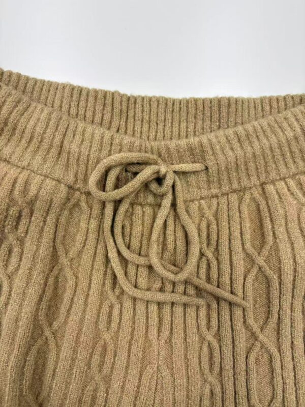 Close-up of a beige knitted sweater featuring a ribbed neckline and a drawstring tie at the waist, showcasing warm, comfortable winter fashion.